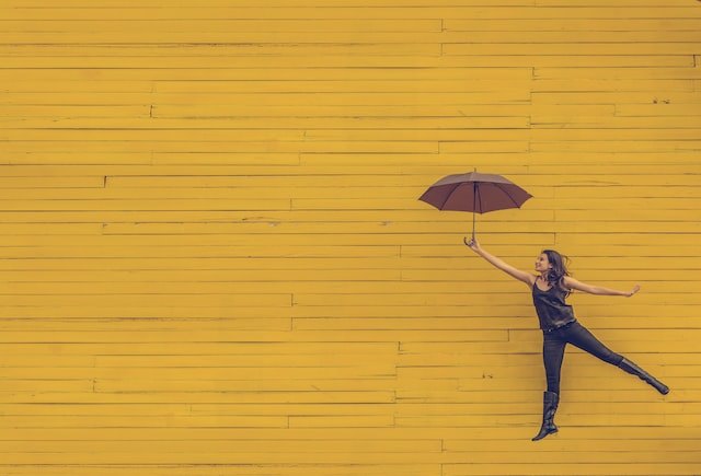Woman jumping while holding an umbrella over a yellow brick background