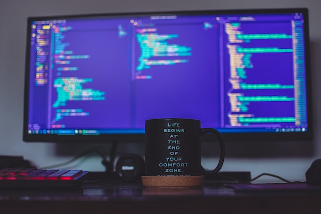Mug with motivational message in front of monitor with code, by Tudor Baciu